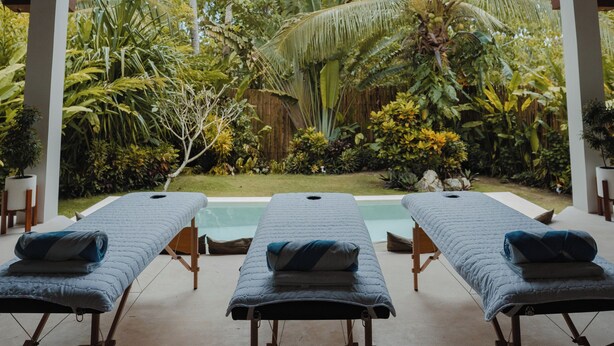 A spa area with three massage tables, a thatched roof, and a view of tropical vegetation.