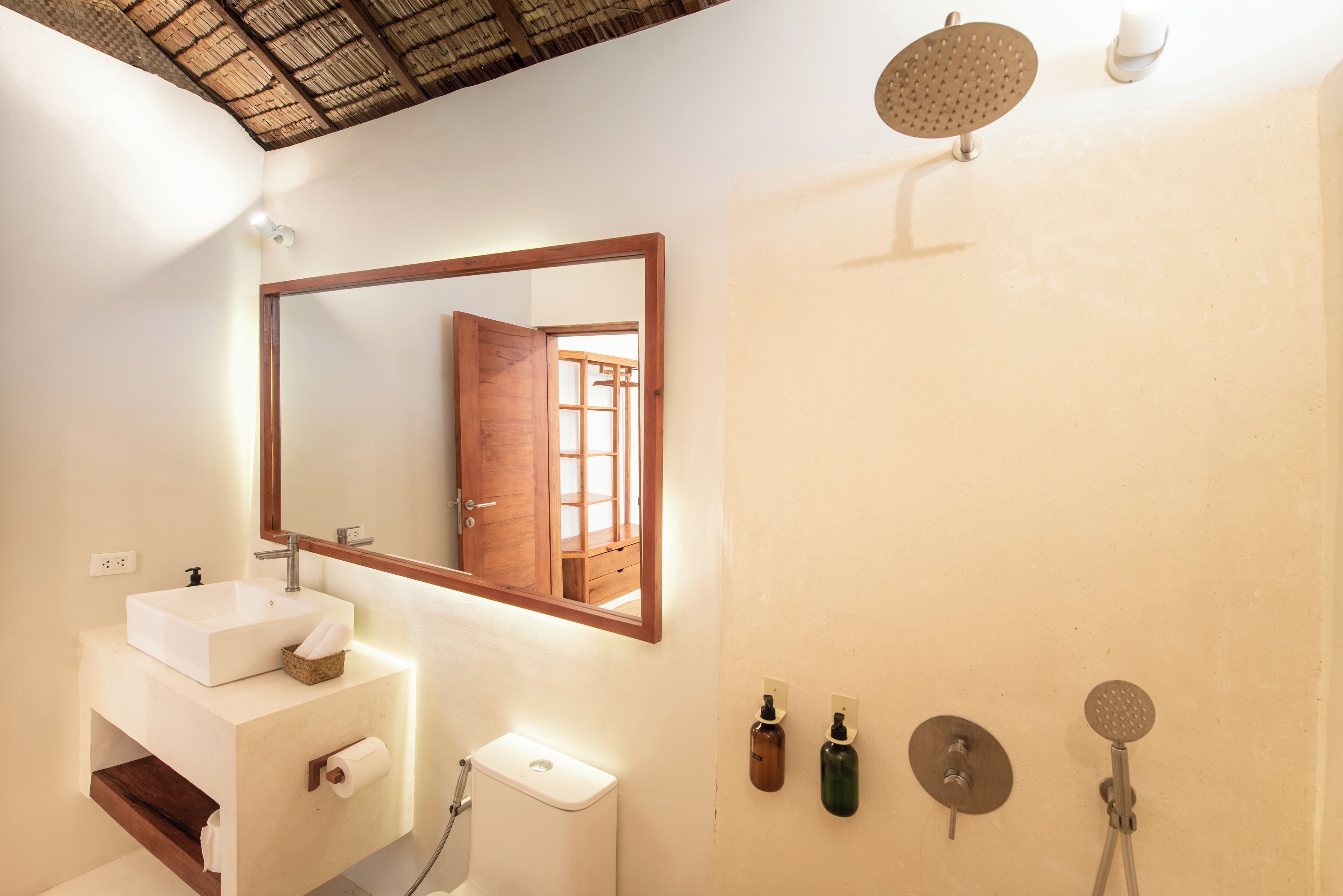 A bathroom with a white sink, a mirror, a toilet, and a shower area.