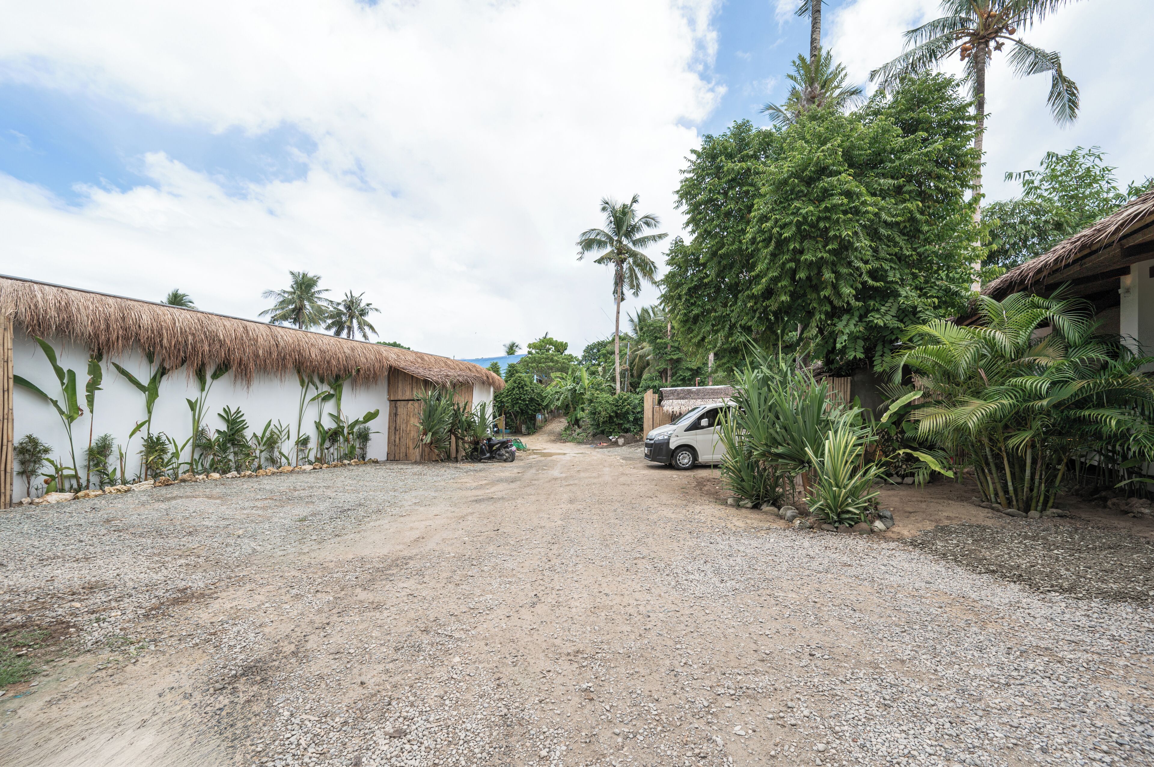 A rural setting with a dirt road, thatched-roof buildings, and tropical vegetation.