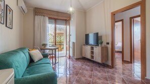 A living room with a green sofa, a TV on a wooden cabinet, and a dining area with a table and chairs. - HOUSE OF SONJA (Viterbo)