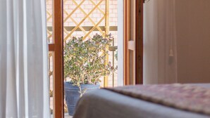 A room with a bed, a potted plant, and a view of a brick wall and lattice outside. - HOUSE OF SONJA (Viterbo)