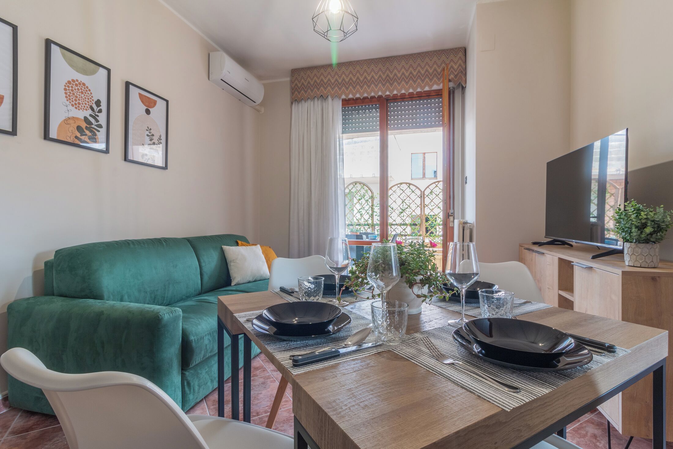 Ein modernes Wohnzimmer mit einem grünen Sofa, einem Esstisch für zwei Personen und einem Fernseher auf einer Holzkommode.