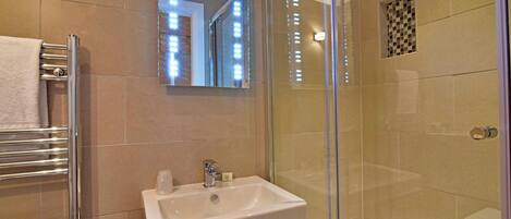 A modern bathroom with a glass-enclosed shower, a white sink, and a towel rack.