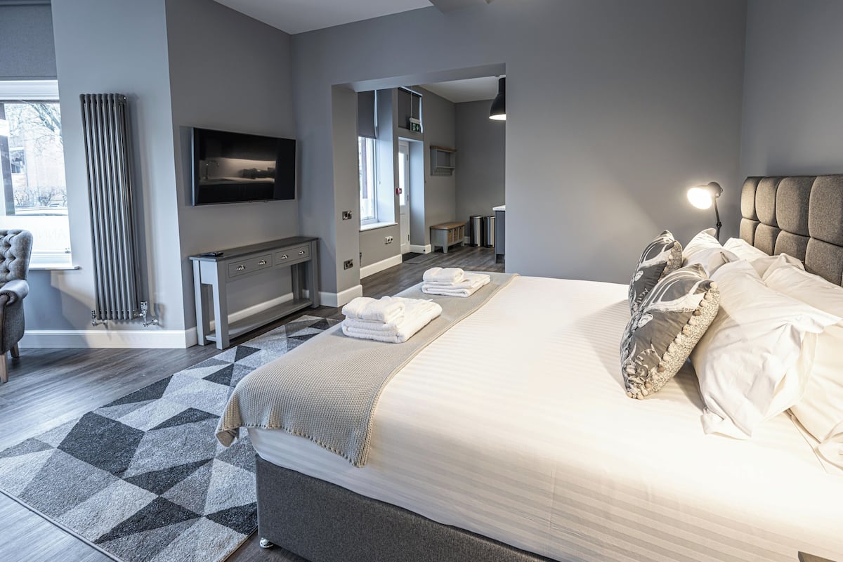 Une chambre d’hôtel moderne dotée d’un grand lit, d’une télévision à écran plat, d’un bureau et d’un coin salon avec un fauteuil.