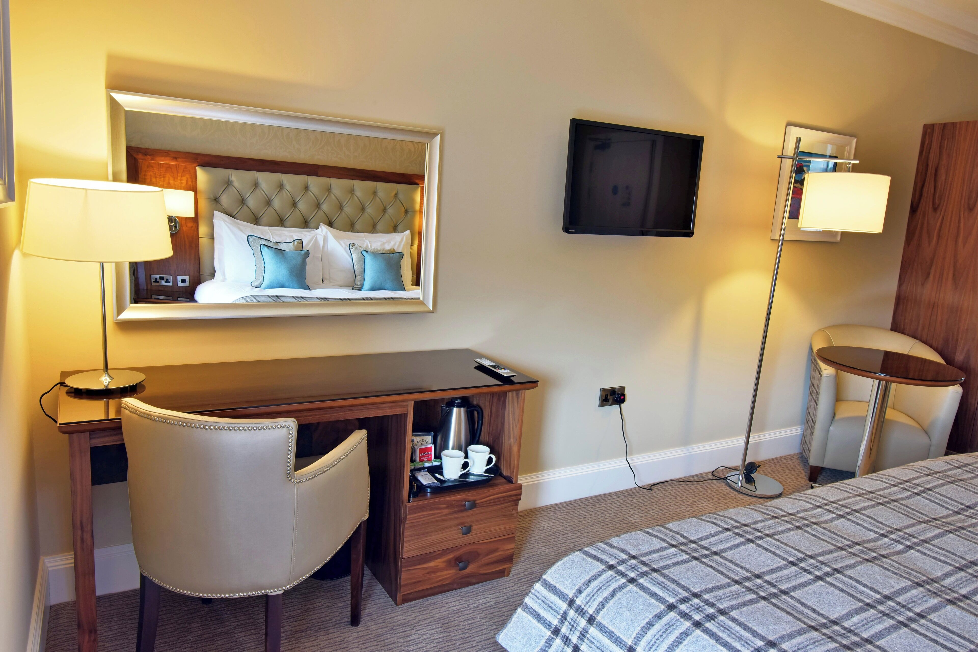 Une chambre d’hôtel équipée d’un lit, d’un bureau, d’une chaise, d’un téléviseur à écran plat, d’une lampe et d’une table de chevet avec une machine à café et des tasses.