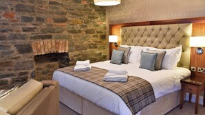 Un letto rifatto con una coperta a quadri, una parete in pietra e una testiera in legno.
