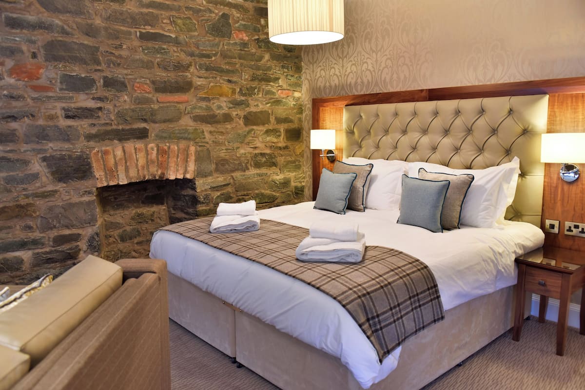 Un lit bien fait, recouvert d’une couverture à carreaux, avec un mur en pierre et une tête de lit en bois.