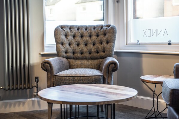 A tufted armchair with a cushioned seat and backrest, positioned next to a round wooden table with a metal base. - The Townhouse Aberfeldy (Aberfeldy)