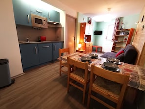 Una cucina compatta con mobili blu, un forno a microonde e un'area pranzo con un tavolo apparecchiato per due.