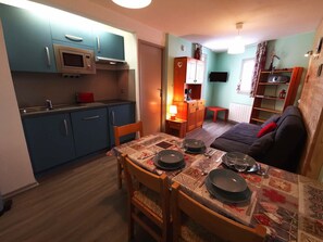 Une cuisine compacte avec des meubles bleus, un four à micro-ondes et un coin repas avec une table dressée pour deux personnes.