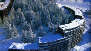 Ein schneebedecktes Gebäude mit kreisförmigem Grundriss, umgeben von dichtem Wald.