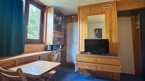 Ein kleines Zimmer mit einem Holztisch, einem Stuhl, einem Fernseher und einem Kühlschrank.