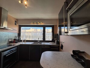 A modern kitchen with a large window, stainless steel appliances, and a marble countertop.