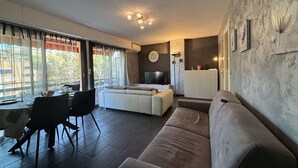 A modern living room with a sofa, dining area, and a TV. - 2-room apartment with air conditioning in Cavalaire-sur-Mer (Cavalaire-sur-Mer)