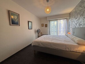 A bedroom with a bed, a ceiling fan, a window with curtains, and a wall-mounted light fixture.