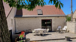 Een gebouw met een pannendak, een terras met een tafel en stoelen, en potplanten.