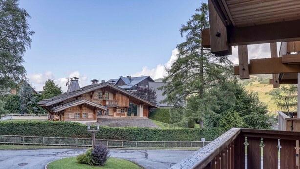 Un chalet en bois doté d’un balcon donnant sur une allée circulaire et un petit jardin.