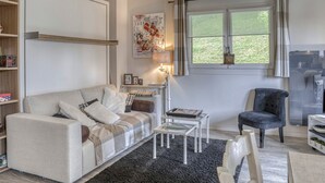 Un salon confortable avec un canapé, une petite table basse, un fauteuil et une fenêtre avec des rideaux.