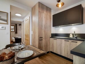 A modern kitchen with wooden cabinets, a black countertop, and a dining area with a table set for two. - Charming T2 apartment in Les Saisies, near slopes (Les Saisies)
