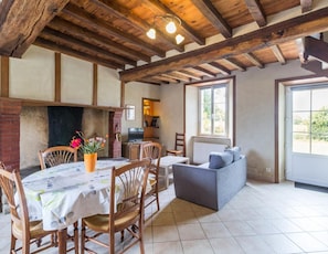 A dining area with a table set for four, wooden chairs, a sofa, and a fireplace. - House with Garden, Pets allowed (Hauteville-la-Guichard)