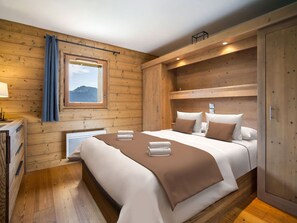 Un dormitorio de cabaña de madera con una cama grande, una ventana con vista a las montañas y un armario de madera.