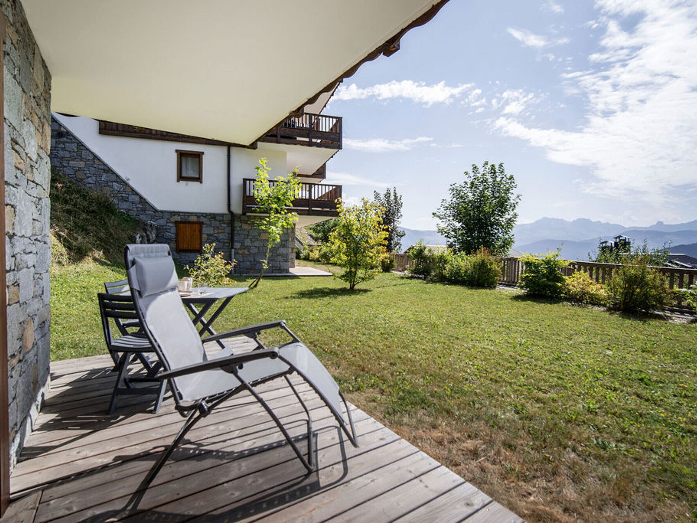 Una terraza de madera con mobiliario exterior, un muro de piedra y vistas a montañas.