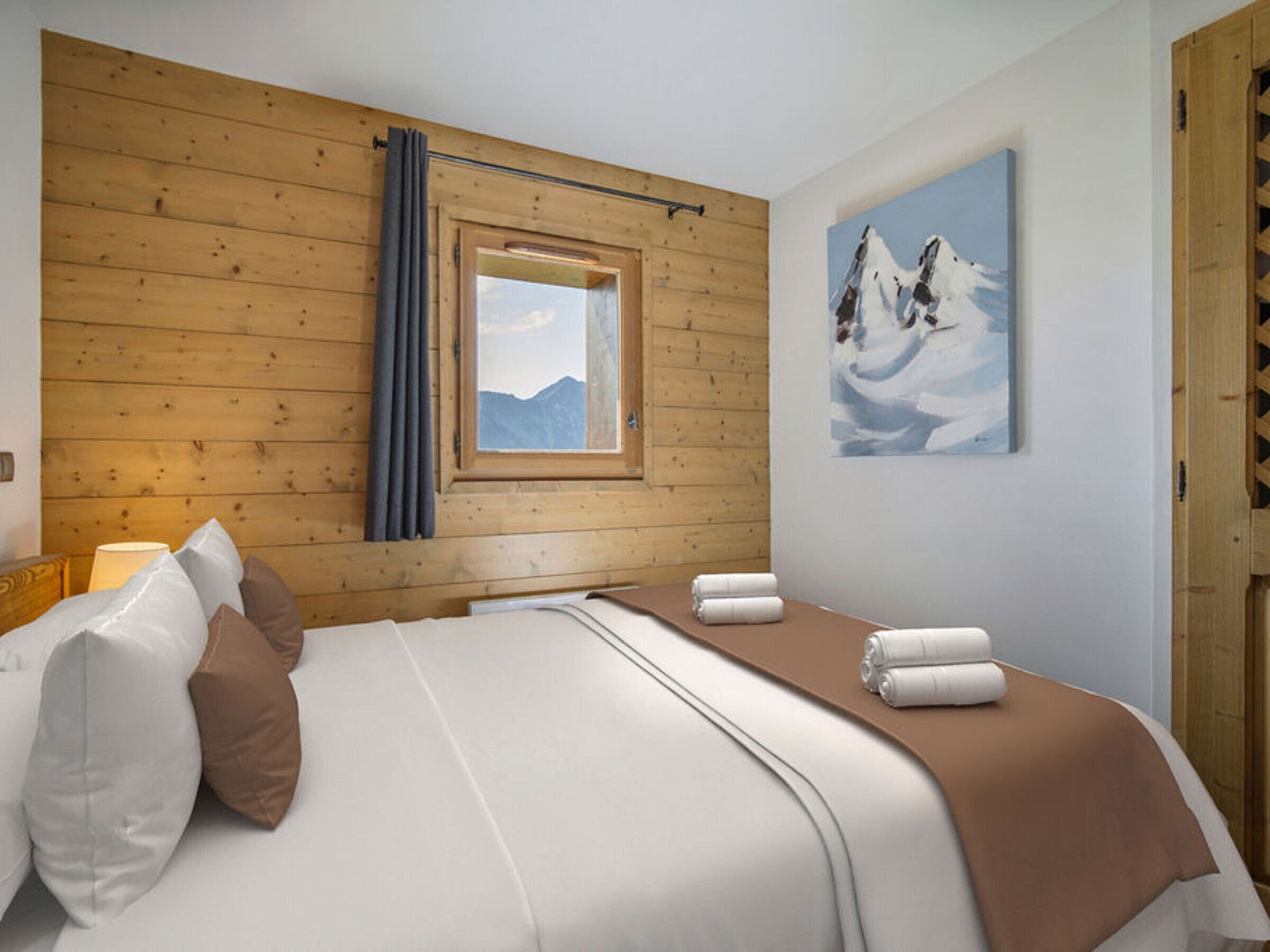 A hotel room with a wooden wall, a window with a mountain view, a bed with white and brown bedding, and a painting of a horse on the wall.