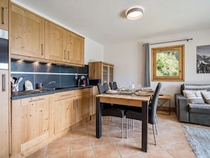 Una cocina moderna con armarios de madera, una mesa de comedor preparada para cuatro personas y un sofá gris en la sala.