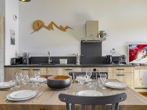 Una cocina moderna con una mesa de madera para seis comensales, horno empotrado y un reloj grande en la pared.