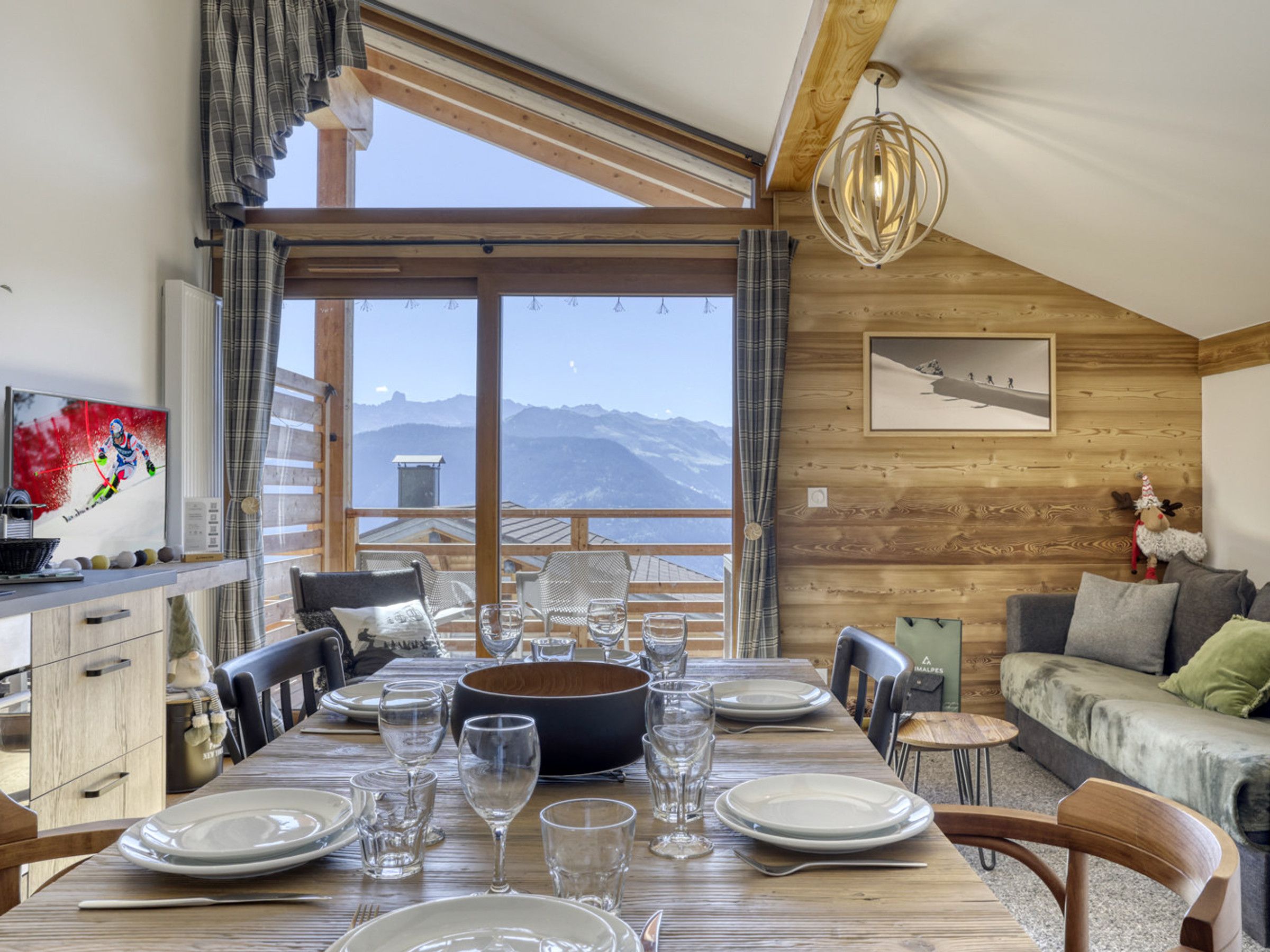 A dining area with a wooden table set for six, a sofa, and a view of mountains.