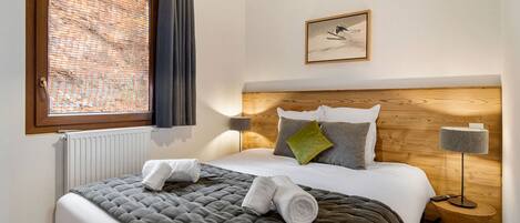 A neatly made bed with a grey quilt, a wooden headboard, and a bedside table with a lamp.