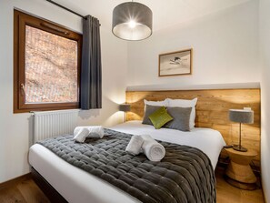 Una cama bien hecha con un edredón gris, un cabecero de madera y una mesita de noche con una lámpara.