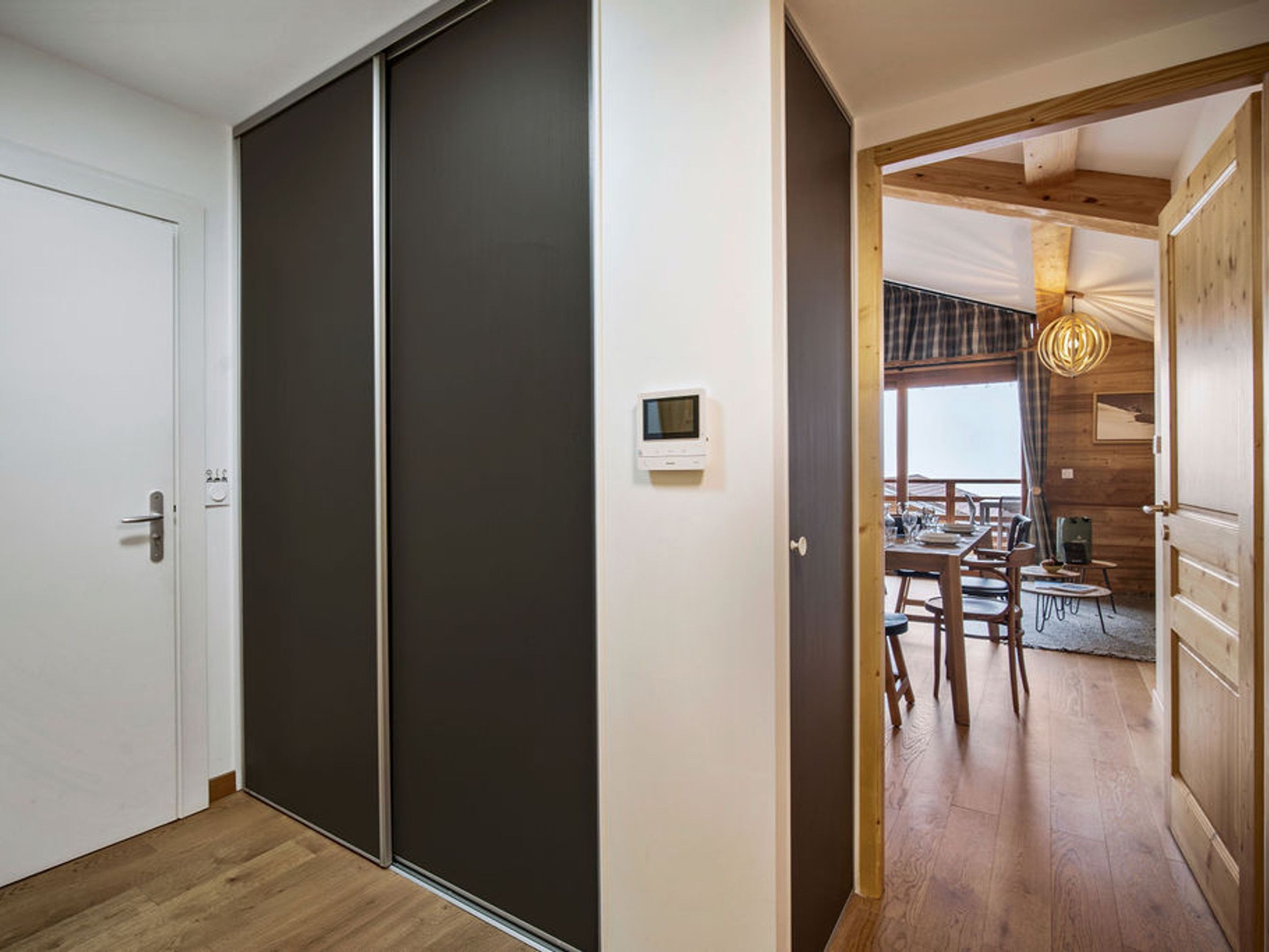 A modern interior with a sliding door, a dining area with wooden furniture, and a visible thermostat on the wall.