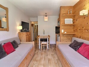 A cozy room with wooden walls, a wooden floor, a sofa, a dining table, and a TV.
