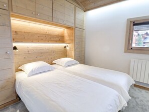 A room with two beds, wooden panel walls, a window, and a radiator.