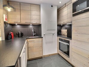 Uma cozinha moderna com armários de madeira, bancada preta, forno embutido e uma geladeira Siemens.