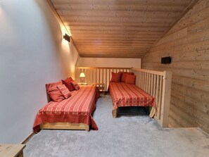 Um quarto pequeno e acolhedor, com duas camas, paredes de madeira, teto inclinado e uma luminária de cabeceira.