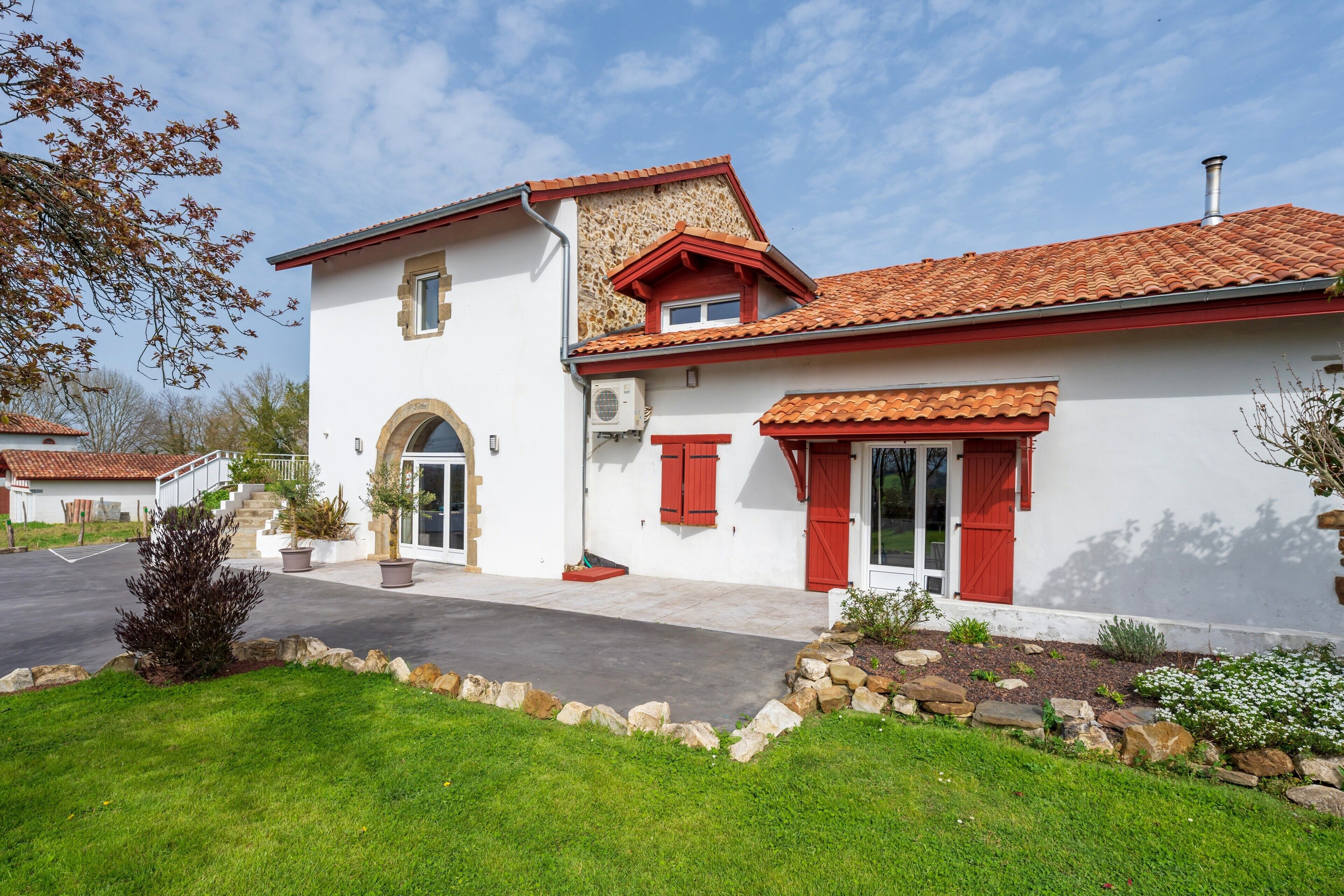 A two-story house with a red-tiled roof, a white exterior, and a stone facade.