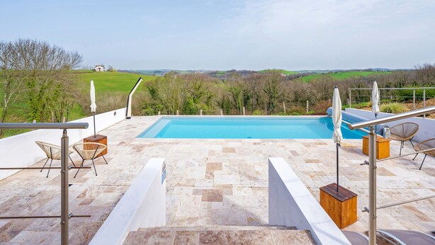 Une piscine sur le toit offrant une vue sur la campagne, des espaces de détente en plein air et une rambarde en métal.