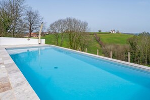 Ein rechteckiger Swimmingpool mit einer glatten, blauen Wasseroberfläche, umgeben von einer weißen Mauer und einem Holzzaun.