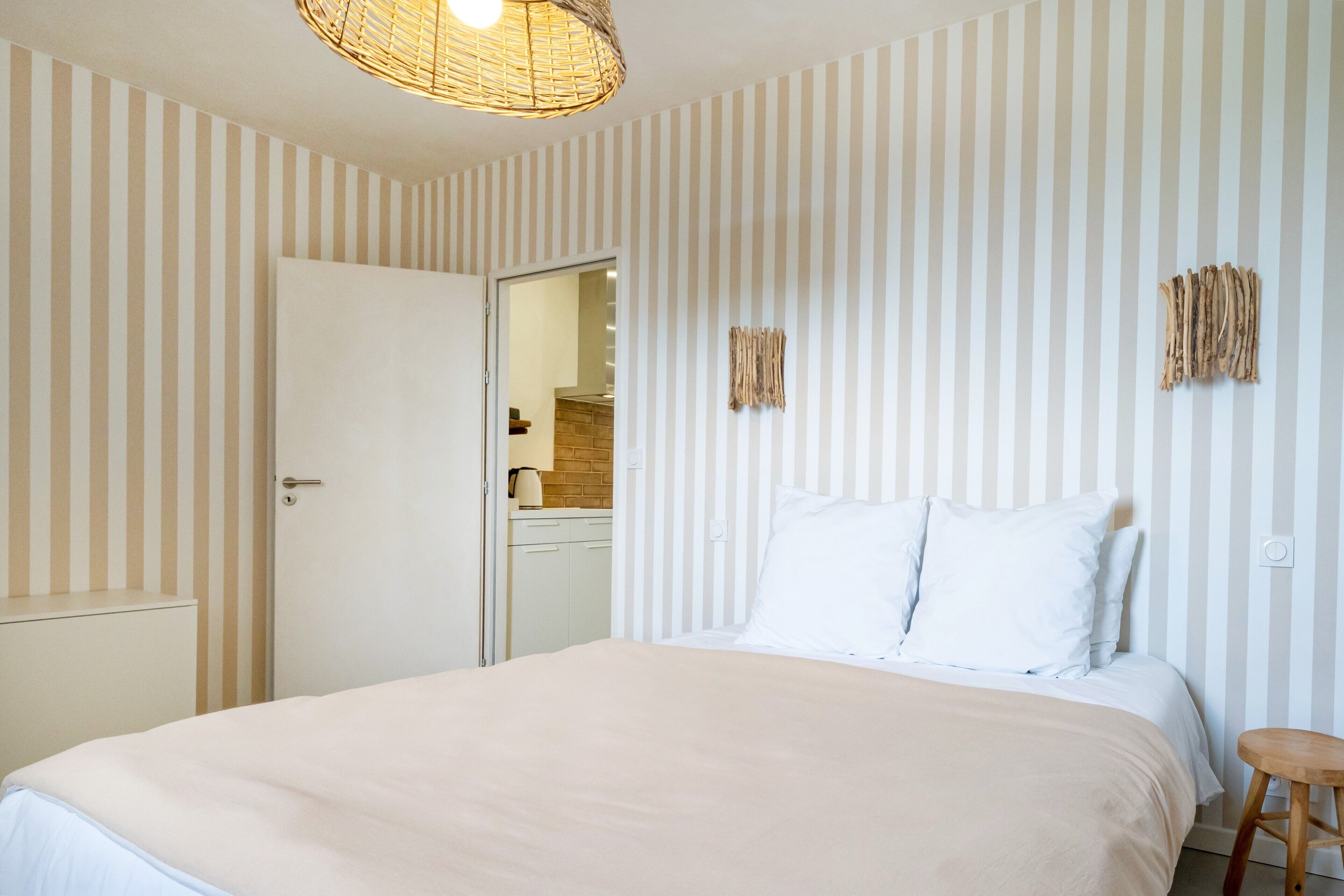 Ein Schlafzimmer mit einem Bett, einem hölzernen Hocker und einer Tür zu einem Badezimmer.