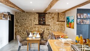 Un comedor con paredes de piedra, vigas de madera, una estantería para vinos y un frutero.