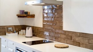 Una cocina con cubierta blanca, extractor de acero inoxidable, cafetera, tableta y tabla de cortar de madera.
