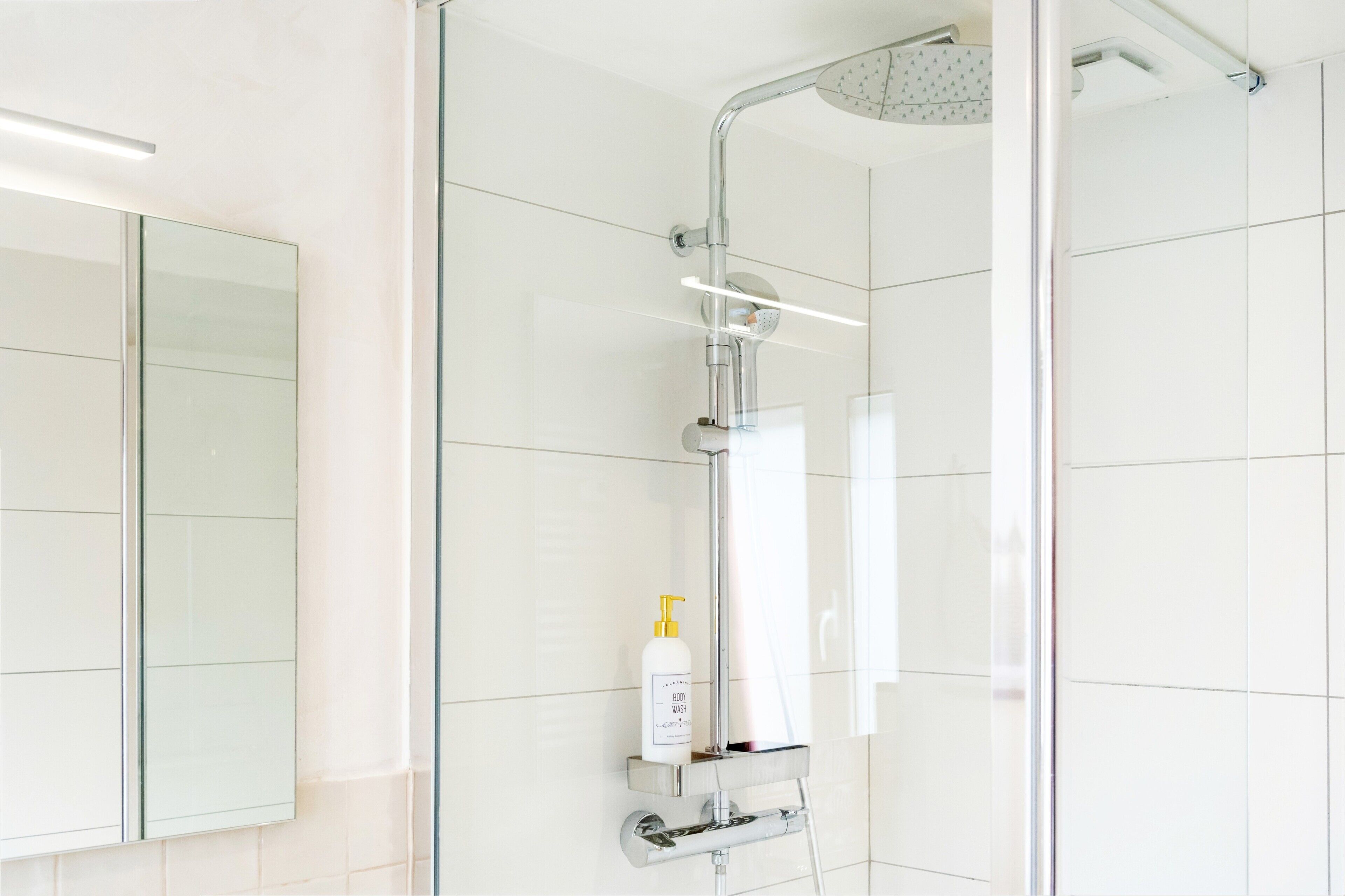 Un baño moderno con cabina de ducha de vidrio, dispensador de jabón de pared y espejo.