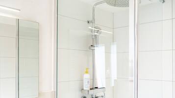 Un baño moderno con cabina de ducha de vidrio, dispensador de jabón de pared y espejo.