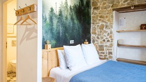 Un dormitorio con cama, cabecero de madera, pared de piedra y un mural con motivos de bosque.