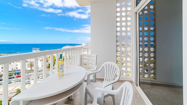 A balcony with a white table and chairs, a bottle of water, and a glass of wine.