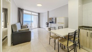 A modern room with a balcony, a dining table with chairs, a TV, and a sofa.