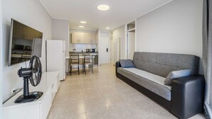 A modern apartment with a kitchenette, a sofa, a TV, and a fan.