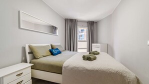 A bedroom with a bed, a bedside table, a dresser, and a window with curtains.